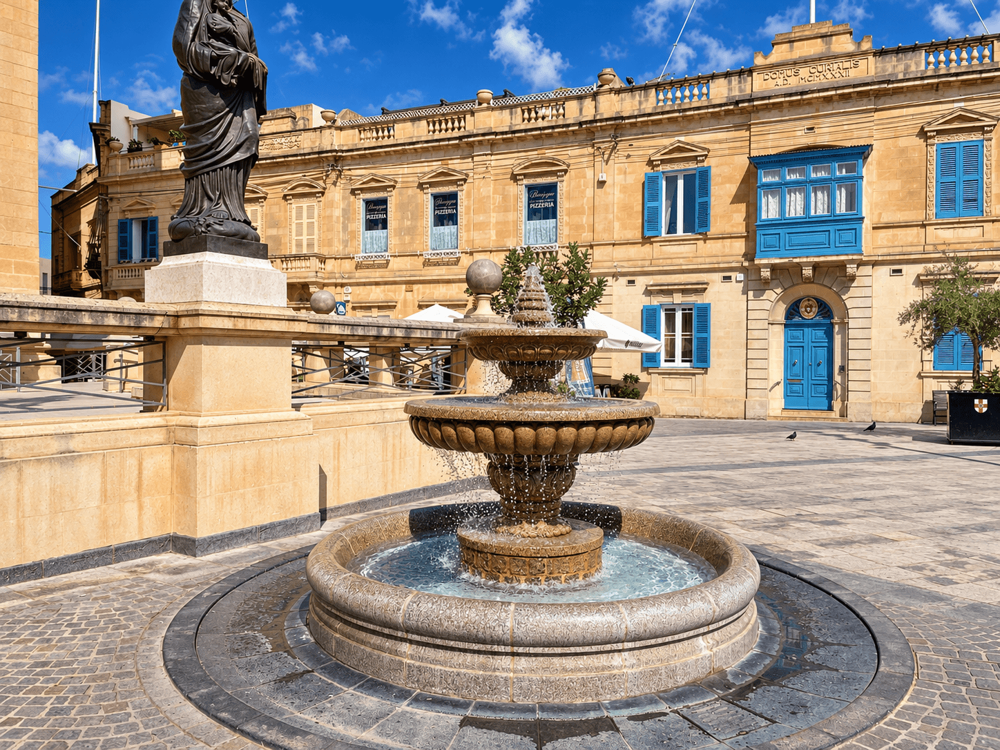 Rotunda showing its limestone columns and entranceStone fountain in Mosta square with traditional limestone buildings and blue shutters